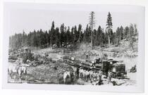 Logging scene with men standing around a train engine