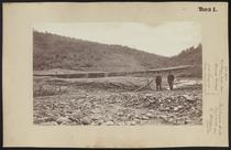 Five men stand near log dam in dry river bed