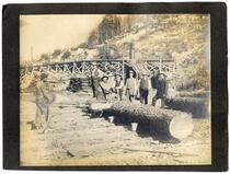 Men observing a logger cutting a log with a steam-powered saw